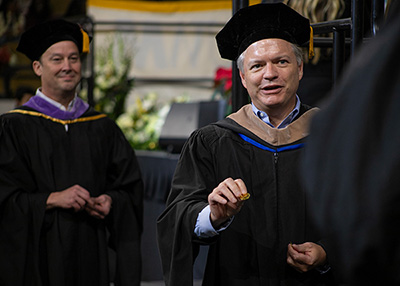 Alumni Association Board Members Chad Wright and Scott Conger hand out coins during graduation